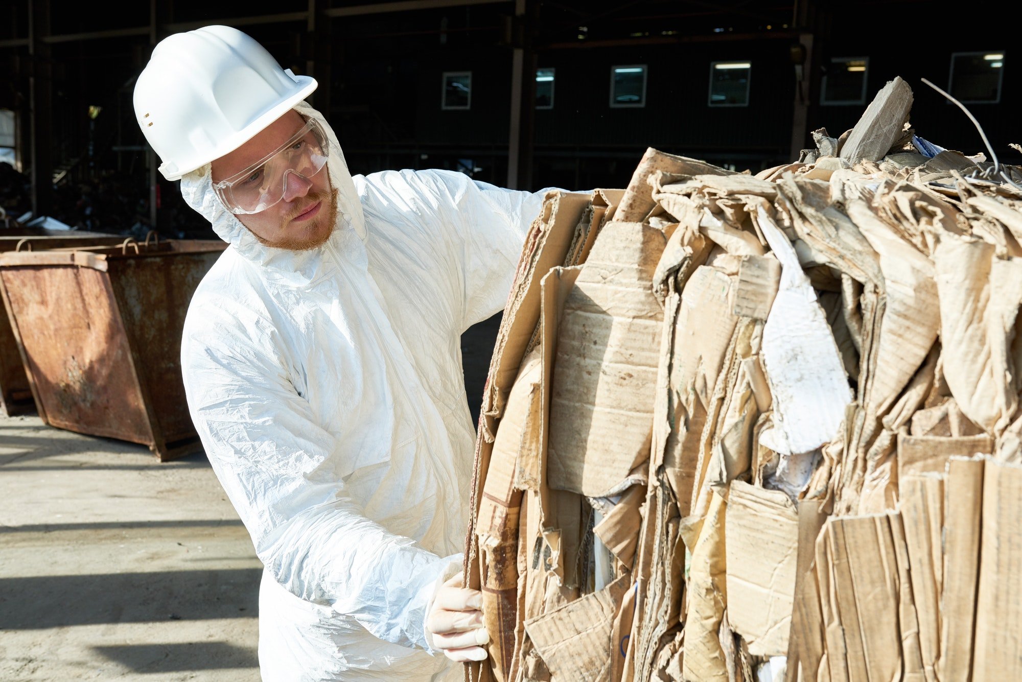 Worker in Hazmat Suit Sorting Cardboard at Recycling Factory